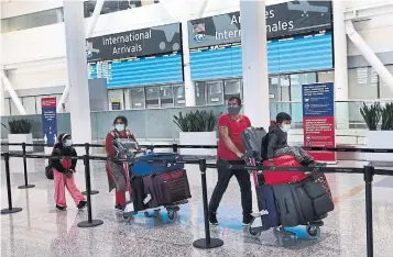  ?? RICHARD LAUTENS TORONTO STAR ?? A family from Delhi arrives at Pearson airport Monday and waits in line for the shuttle bus to their quarantine hotel. New quarantine rules require air travellers to call either a toll-free or collect number to book their hotel. There’s no online booking system in place.