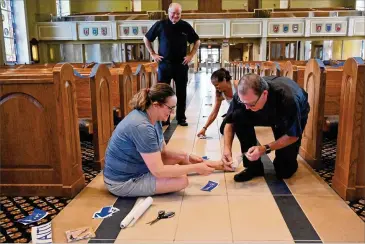  ??  ?? Mary Beth McKenna (left), director of religious education, Deacon John Puetz (right) and youth minister Rita Anderson apply guides on the floor as Father Paul Flood preps for Mass today at St. Benedict Catholic Church.