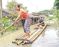  ??  ?? A woman steers a bamboo-raft along a flooded road.