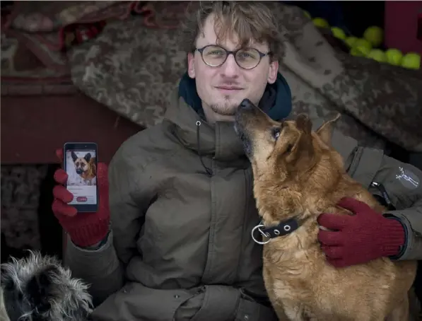  ?? Mindaugas Kulbis/Associated Press photos ?? Vaidas Gecevicius, who developed an app helping to match stray dogs with potential owners, poses for a picture with a dog and shows this dog’s profile on the app in Vilnius, Lithuania. A group of enthusiast­s have launched an app that helps match aspiring dog owners with stray dogs.