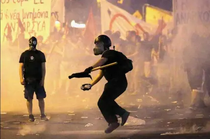  ?? Yannis Behrakis/Reuters ?? A masked youth hurls a projectile at riot police during clashes Wednesday in Athens, Greece