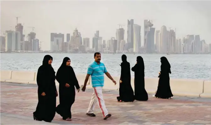  ??  ?? DOHA: With the new high-rise buildings of downtown Doha in the background, Qatari women and a man enjoy walking by the sea in Doha. — AP