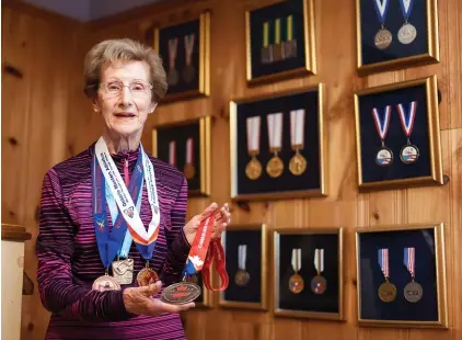  ??  ?? Jean Horne holds and wears medals won as a race walker. On the wall are medals from her running days.