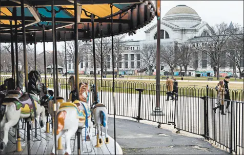  ?? BRENDAN SMIALOWSKI/GETTY-AFP ?? People pass an empty merry-go-round and the closed Smithsonia­n Natural History Museum on Saturday in Washington.