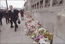  ??  ?? Conservati­ve MP Tobias Ellwood walks past floral tributes to victims of Wednesday’s attack outside the Houses of Parliament in London on Friday.