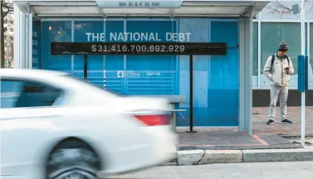  ?? OLIVER CONTRERAS/THE NEW YORK TIMES ?? A sign with a running tally of the national debt hangs inside a bus stop shelter last month in Washington, D.C. On Wednesday, the Congressio­nal Budget Office issued its fiscal forecast for the upcoming decade.