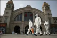  ?? ASSOCIATED PRESS FILE PHOTO ?? Workers in protective suits walk past the Hankou railway station on the eve of its resuming outbound traffic in Wuhan in central China’s Hubei province.