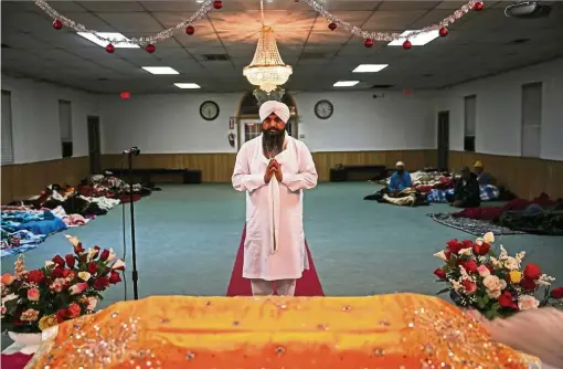  ??  ?? Nirmal Singh conducting a morning prayer ritual as evacuees sleep in the background at the temple.