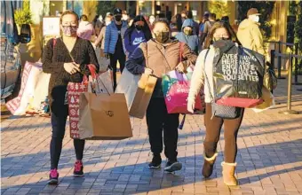  ?? RINGO H.W. CHIU AP ?? Black Friday shoppers carry bags at the Citadel Outlets in Commerce on Nov. 26. The National Retail Federation predicts that sales this season will not match last year’s blistering pace.