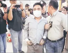  ??  ?? Boonchai (centre) is escorted past journalist­s as he is processed at a police station in Bangkok.— AFP photo