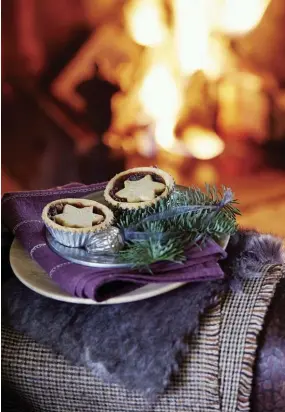  ??  ?? |ABOVE RIGHT| FIRESIDE SWEETS. A plate of mince pie treats from Betty’s sits on the edge of the leather chair. The pies are displayed atop a layer of plum-colored napkins from Denby, spruce sprigs and a silver acorn decoration.