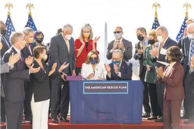  ?? ALEX BRANDON/AP ?? House Speaker Nancy Pelosi of Calif., Senate Majority Leader Chuck Schumer of N.Y., both seated, and Maryland Rep. Steny Hoyer, left of Pelosi, among others, celebrate after signing the $1.9 trillion COVID-19 relief bill Wednesday in Washington.