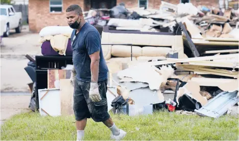  ?? GERALD HERBERT/AP ?? Derek Anthony dumps debris at the curb while gutting his LaPlace, Louisiana, home that was flooded after Hurricane Ida made landfall in late August. Storm damage has some residents debating whether to stay or move.