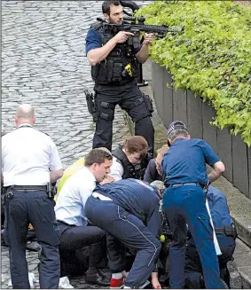  ?? AP/STEFAN ROUSSEAU ?? Armed officers stand on guard Wednesday as emergency workers help a victim outside Parliament in London, where a man drove into pedestrian­s before attacking an officer with a knife. He was then shot.