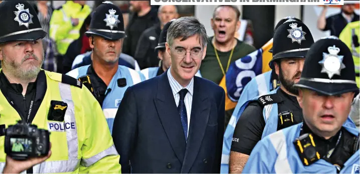  ?? ?? Safety first: Jacob Rees-Mogg receives a protective police guard as he is heckled by protesters on arrival at the Conservati­ve Party conference in Birmingham yesterday