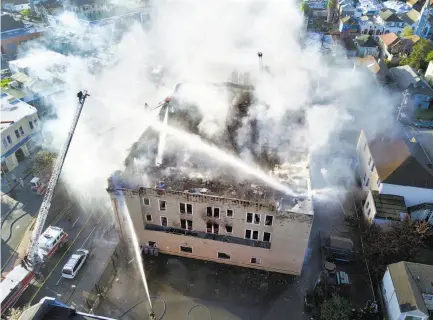  ?? Jim Stone / Special to The Chronicle ?? Firefighte­rs work to put out the fire that erupted on the roof in a troubled transition­al housing building in West Oakland.