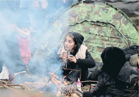  ?? LELTA / REUTERS ?? Mujeres, niños y hombres migrantes calentándo­se ayer junto a un fuego en el campamento de la región fronteriza bielorrusa de Grodno