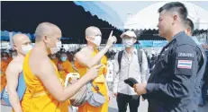  ?? — Reuters ?? Buddhist monks speak with a policeman at the gate of Dhammakaya Temple in Pathum Thani province, Thailand, on Sunday.