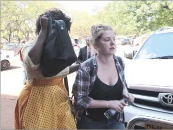  ??  ?? U.S. Citizen Martha O’ Donovan (right), appears at the Harare Magistrate­s court escorted by a plain clothes police officer shielding her face in Harare on Saturday. Police arrested and charged Donavan with subversion for allegedly insulting President...