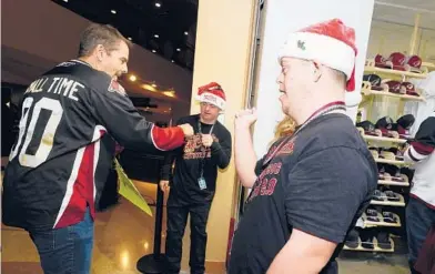 ?? ROSS D. FRANKLIN/AP ?? Matthew Adams, right, and Chase Baird, middle, greet a fan at the entrance to the Arizona Coyotes’ team shop prior to a Dec. 3 game. Adams and Baird were hired through Angels for Higher, a group that helps people with Down syndrome work as greeters.