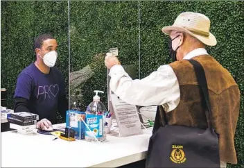  ?? DAMIAN DOVARGANES AP ?? Josh Smart (left) helps customer Eric Hall make a contactles­s purchase through a plexiglass wall at a store in Burbank. On Friday, Los Angeles County announced a new stay-home order as coronaviru­s cases surge.