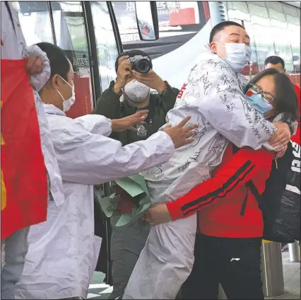  ?? (AP/Ng Han Guan) ?? A medical worker from China’s Jilin Province (in red) embraces a colleague from Wuhan as she prepares to return home at Wuhan Tianhe Internatio­nal Airport in central China’s Hubei Province. Within hours of China lifting an 11-week lockdown in Wuhan, tens of thousands people had left the city by train and plane alone, according to local media reports.