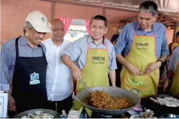  ??  ?? Salahuddin (second right) shows his cooking skill during the ‘Jualan Jimat Belanja Aidil��tri' event at Section 13 Farmers�� Market. — Bernama photo