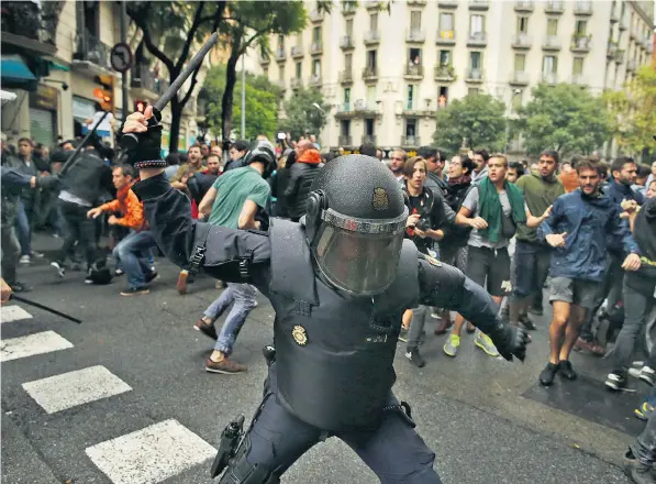  ??  ?? A Spanish police officer in riot gear swings a club against would-be voters near a school assigned to be a polling station by the Catalan government in Barcelona