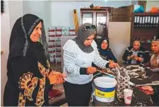  ??  ?? Syrian refugee Sameera Al Salam shows a colleague how to strengthen a paper handbag with glue, at an upcycling workshop in Irbid city, northern Jordan.