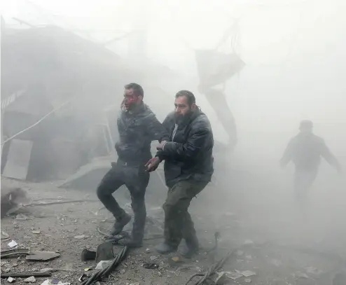  ?? ABDULMONAM EASSA / AFP / GETTY IMAGES ?? A wounded man is helped out of a destructio­n zone following air strikes in Syria on Thursday. A U. S.-led coalition killed more than 100 Assad regime fighters, an attack the Syrian government called “a crime against humanity.”