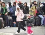  ?? PHILIPPE HUGUEN/AFP ?? A migrant with her child walks past other migrants who are waiting with their luggage to leave the ‘Jungle’ migrant camp in Calais on October 24.