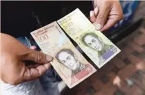  ?? — AFP ?? A man holds the new one hundred thousand-Bolivar-note (R) comparing it to the one hundred note, to show the resemblanc­e between both bills in Caracas.