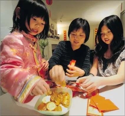  ?? STEVE BOSCH / PNG ?? Anna Bin and daughters Chloe ( left) and Cindy stuff red envelopes with chocolate coins in preparatio­n for Chinese New Year in Vancouver on Wednesday. Bin says she misses the taste of her extended family’s dumplings in Guangzhou, China.
