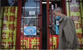  ??  ?? A man walks past a blue sign indicating workers’ Covid vaccinatio­n rates on the door of a printing business in Beijing. Photograph: Leo Ramirez/AFP/Getty Images