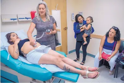  ?? EDDIE MOORE/JOURNAL ?? Sabrina Esquibel lies still as Dr. Wendy Johnson listens to the heartbeat of her unborn child while Myriam Salazar, holding Esquibel’s daughter Milaya, and Ana Morelos look on at La Familia Medical Center.