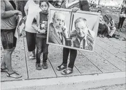  ?? TOMAS MUNITA NEW YORK TIMES ?? Top, Raul Castro looks at his watch in January as he walks with Miguel Díaz-Canel Bermúdez, then Cuba’s vice-president, in Havana, Cuba. Left, a woman holds a poster of Fidel and Raul Castro in 2016.