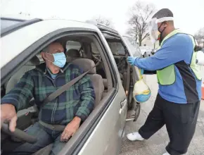  ?? PHOTOS BY MIKE DE SISTI / MILWAUKEE JOURNAL SENTINEL ?? Volunteer Chris Walton, right, chairman of the Democratic Party of Milwaukee County, places a frozen turkey in the minivan of Andrew Parker, of Milwaukee, as part of the COVID-safe turkey drive at the King Community Center at 1531 W. Vliet St. on Tuesday. Hosted by the We Care Crew, the food drive provided Thanksgivi­ng meals and winter resources to families with a goal of serving 2,000 families in a drive-through COVID-safe event.