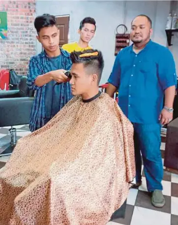  ??  ?? MOHD Rosli (kanan) memerhatik­an pekerjanya mengguntin­g rambut pelanggann­ya di kedainya di The Jangot's Barbershop.