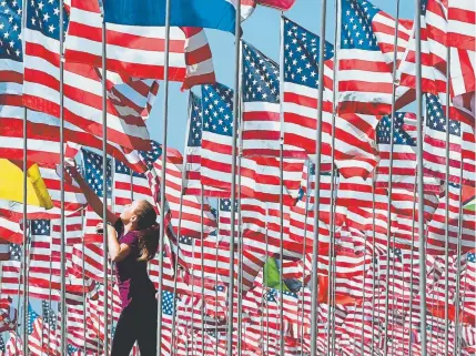  ?? Frederic J. Brown, AFP/Getty Images ?? A girl jumps to touch a flag as people visit the “Waves of Flags” display at Pepperdine University in Malibu, Calif., on Monday, where the display of 2,997 flags commemorat­es victims of the Sept. 11, 2001, terrorist attacks.