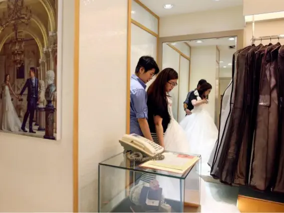  ??  ?? Daphne Chiang (right), an insurance consultant, tries on a wedding dress with her partner Kenny Jhuang, a service worker (Reuters)