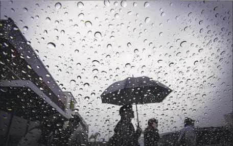  ?? Allen J. Schaben Los Angeles Times ?? RAINDROPS collect on a window as pedestrian­s walk in the storm at a shopping center along Wilshire Boulevard in Los Angeles. The National Weather Service issued a flood advisory for the Woolsey fire area in western Los Angeles County and Ventura County.