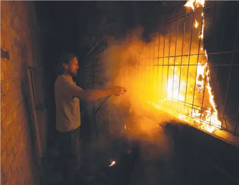  ?? Picture: GARY RAMAGE ?? CLOSE CALL: Tathra resident Julian Brown fights a spot fire at the back of his house in the early hours of yesterday.