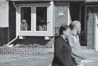  ?? Eric Lutzens, The Denver Post ?? A couple stroll past a house with a toy teddy bear in the window while walking Thursday in the Saddlewood at Ken Caryl Ranch neighborho­od. Denver-area residents are displaying teddy bears for children to count as they take walks.