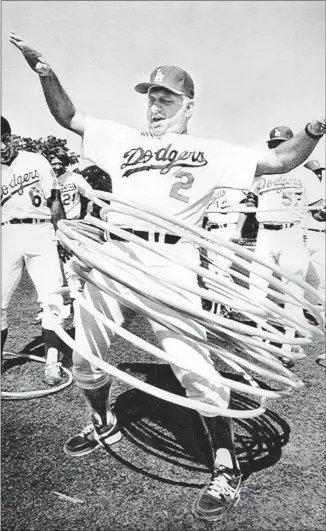 ?? Jayne Kamin Los Angeles Times ?? TOMMY LASORDA tries nine hula hoops as Steve Garvey, left, and other Dodgers get a laugh in spring 1982. Lasorda spent 71 years with the Dodgers and his enthusiasm remained strong.