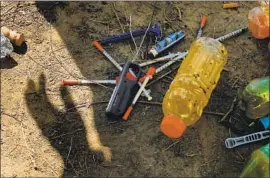  ??  ?? A WORKER stands over syringes and other items left behind at the Echo Park homeless camp Friday. Homeless advocates had deemed the park a community.