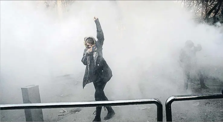  ?? STR / EFE ?? Una joven manifestan­te se protege de los gases lacrimógen­os lanzados por la policía para dispersar una manifestac­ión alrededor de la Universida­d de Teherán