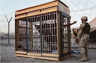  ?? John Moore/Associated Press file ?? A detainee in an outdoor solitary confinemen­t cell talks with a military police officer at the Abu Ghraib prison on the outskirts of Baghdad in this 2004 photo.