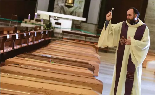  ?? PIERO CRUCIATTI/AFP ?? El padre italiano Marcello Cagliari bendice decenas de féretros en la iglesia de San Giuseppe, ubicada en la localidad de Seriate. En estos días, el templo se ha convertido en una especia de funeraria improvisad­a.