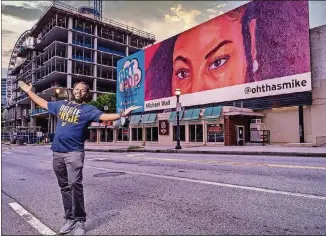  ?? COURTESY OF MARK ALBERHASKY ?? Michael Wall proudly shows his billboard near Centennial Park.