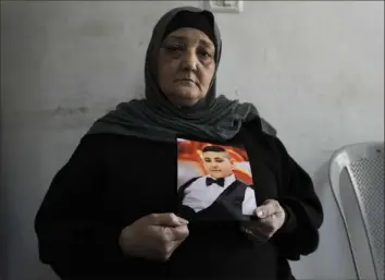 ?? Mahmoud Illean/Associated Press ?? Rawiya Halhouli with a photo of her slain son Rami in their home in a refugee camp in east Jerusalem, March 17. Rami was shot by an Israeli police officer while launching a firework.